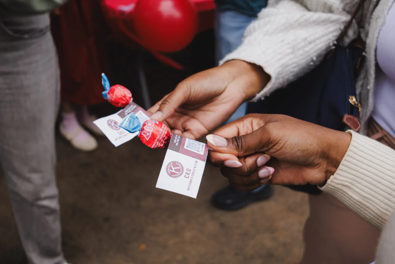 A member handing a candy and a Circle K card to a student