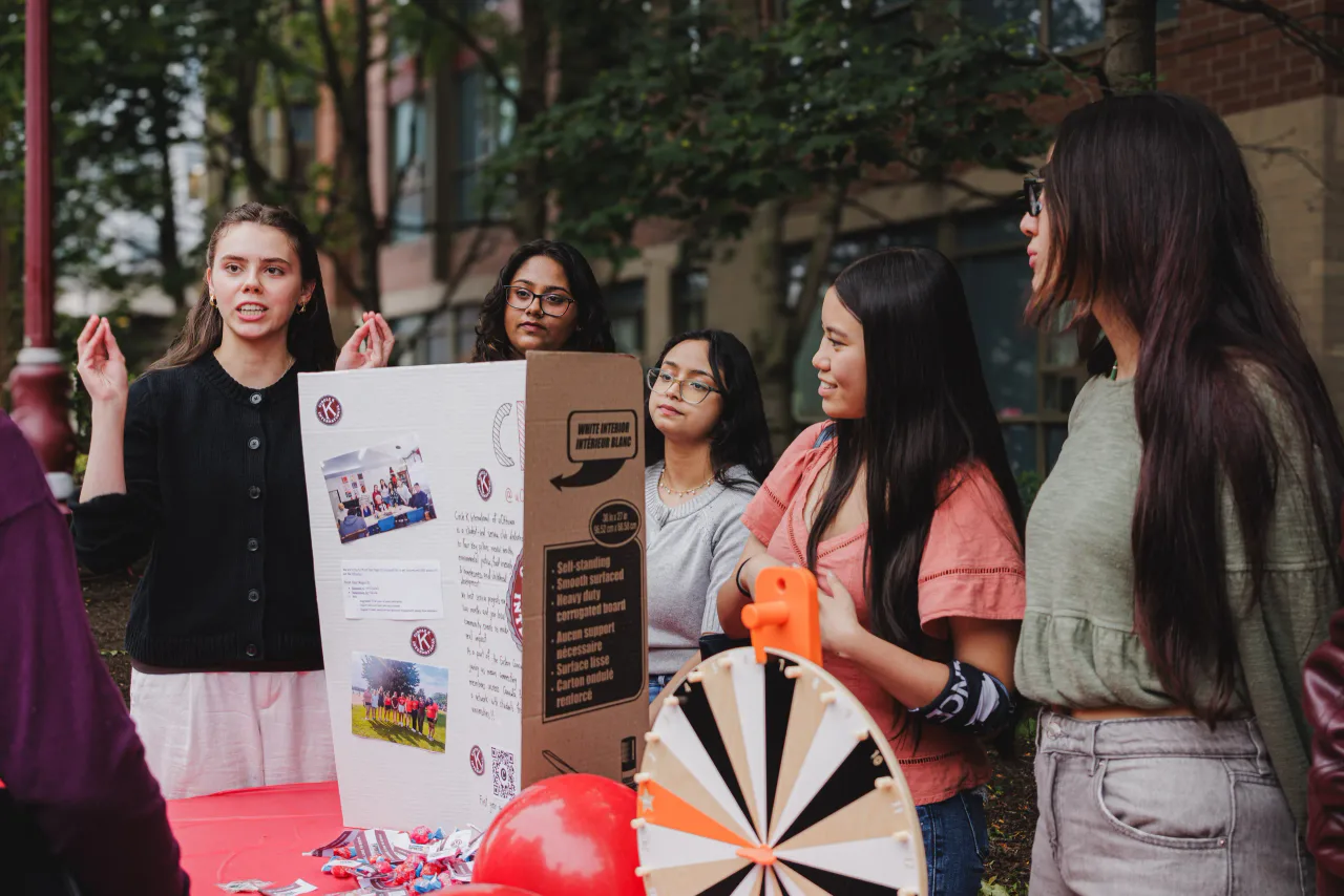 A member explaining Circle K to students beside the prize wheel